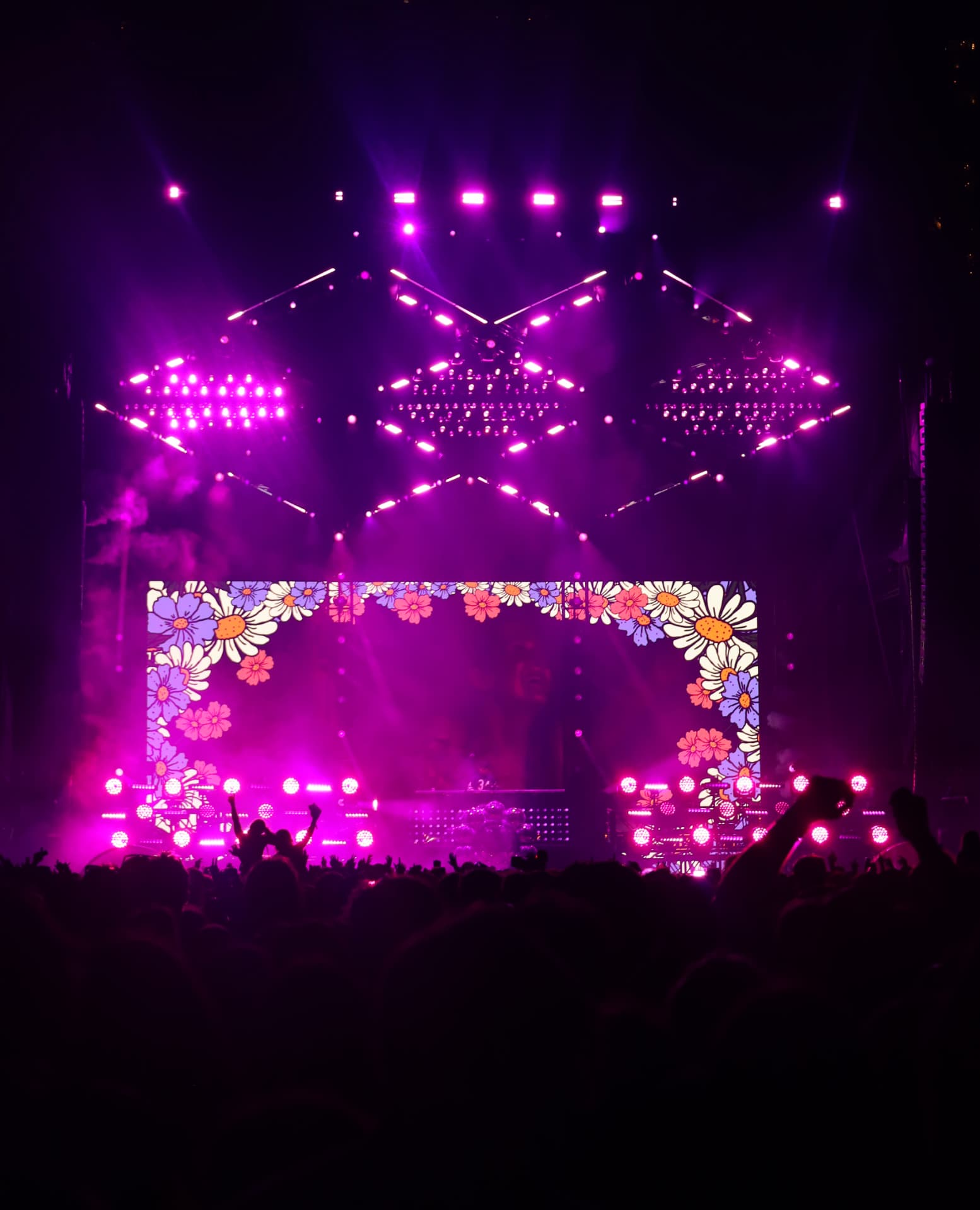 Main stage framed by animated daisies under magenta beams and raised hands