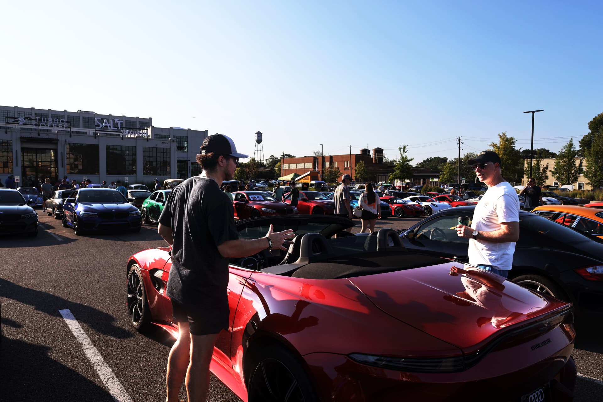 Crowded outdoor car meet with enthusiasts gathered around supercars