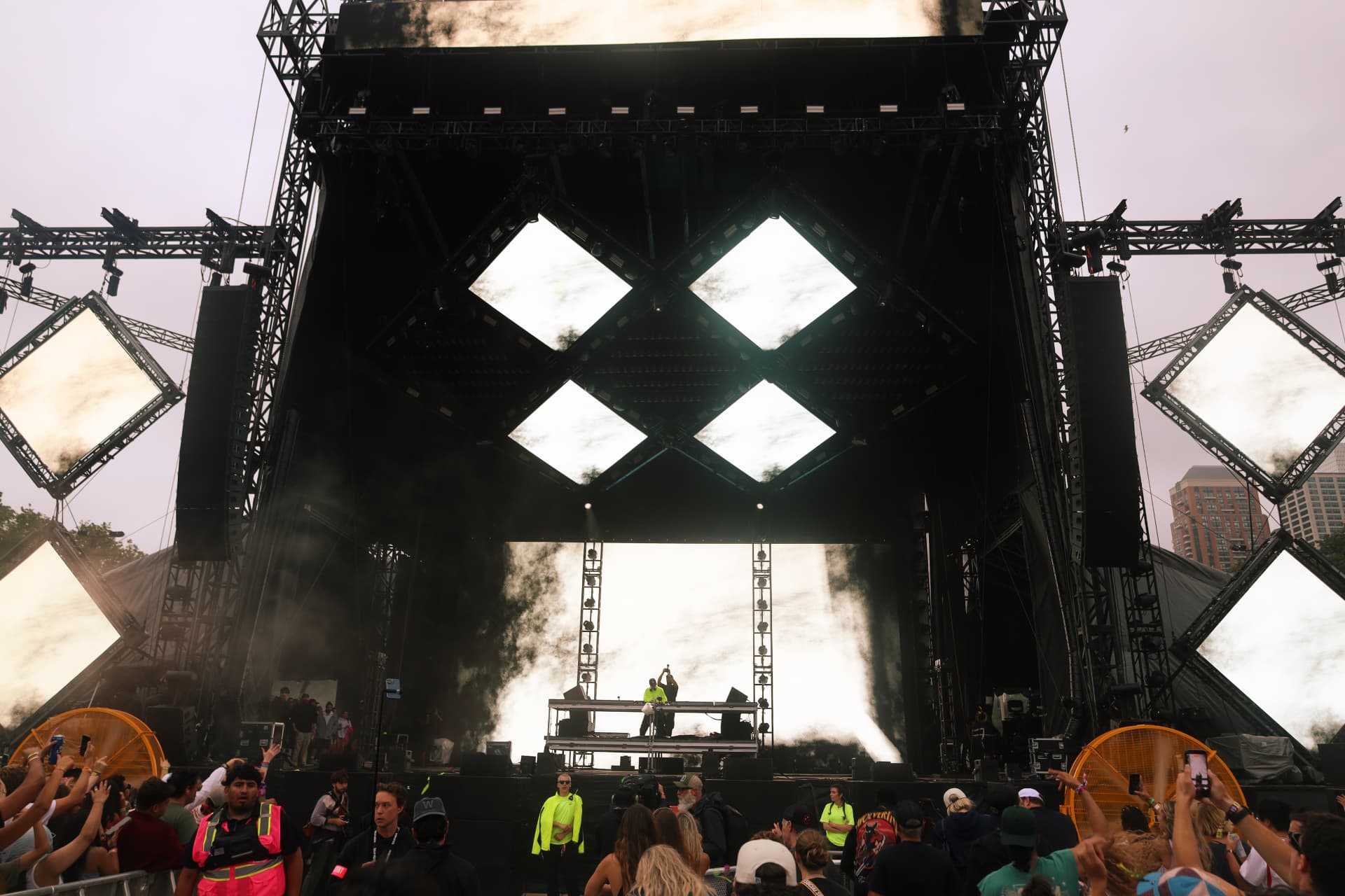 Wide view of the main stage with DJ, crowd and smoke plumes at dusk