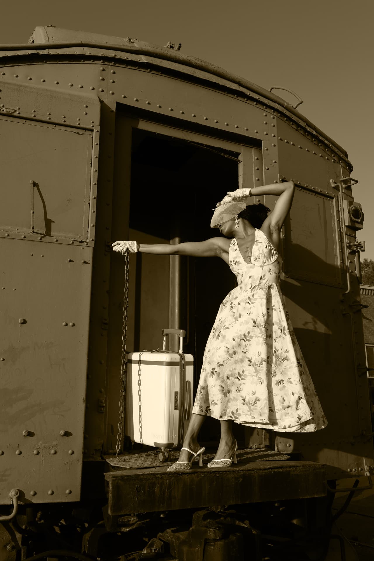 Sepia portrait of a model posed with a suitcase on a vintage rail car platform