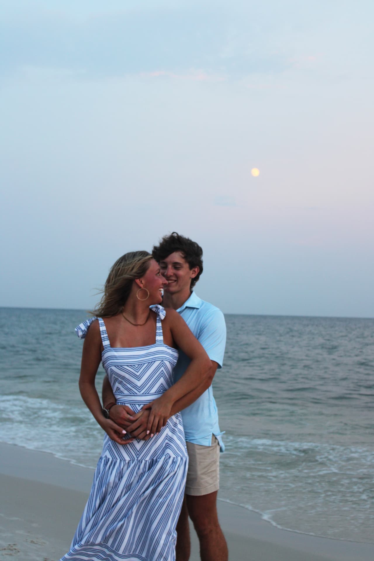 Couple laughing in an embrace at the water's edge beneath a rising moon