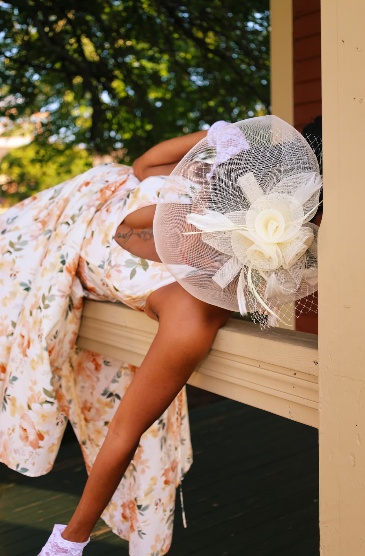 Floral gown draped over a porch railing beneath a feathered veil hat