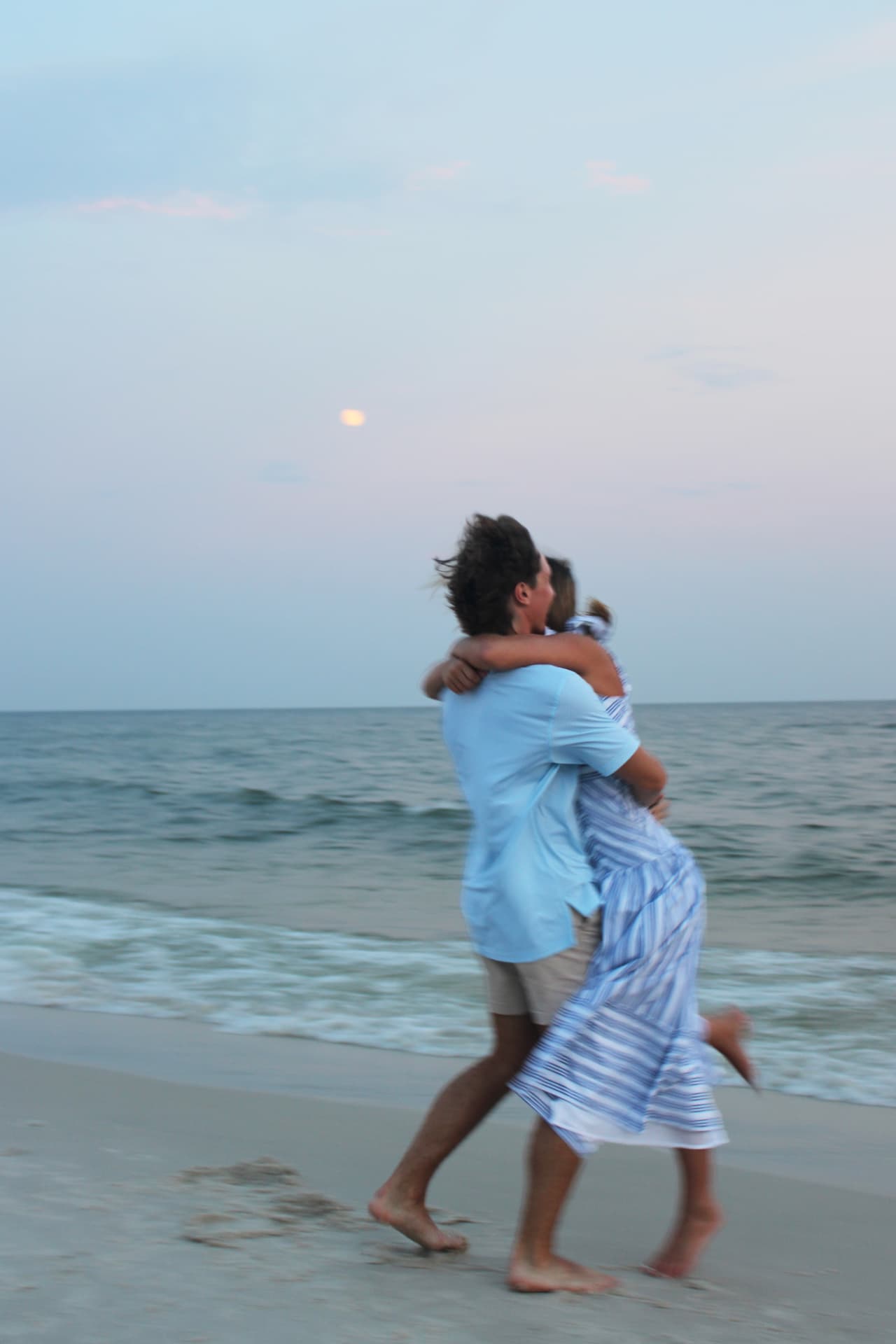 Couple lifted in an embrace beneath the moon at the water's edge