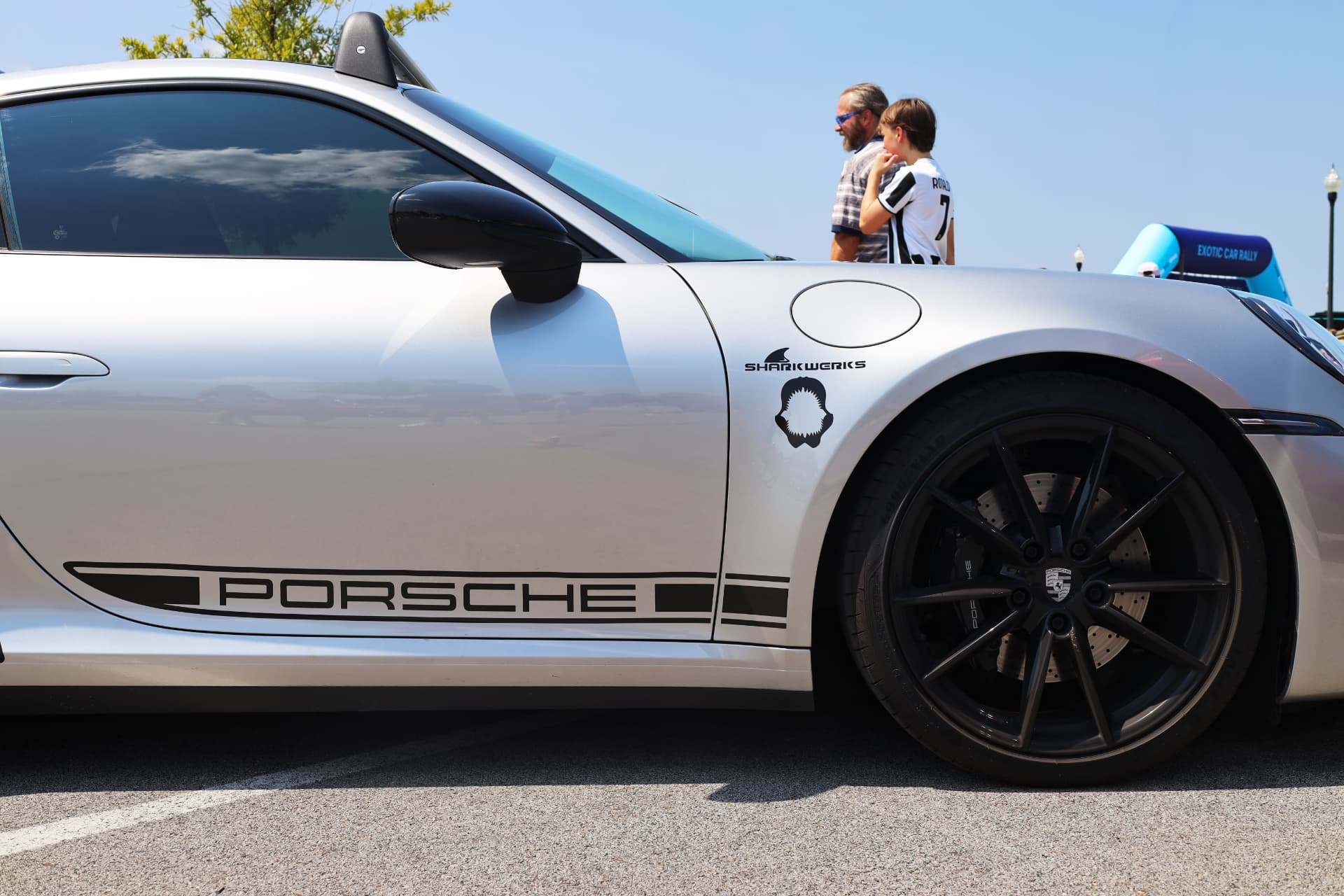Silver Porsche 911 with Sharkwerks decal and black wheels at an exotic car rally