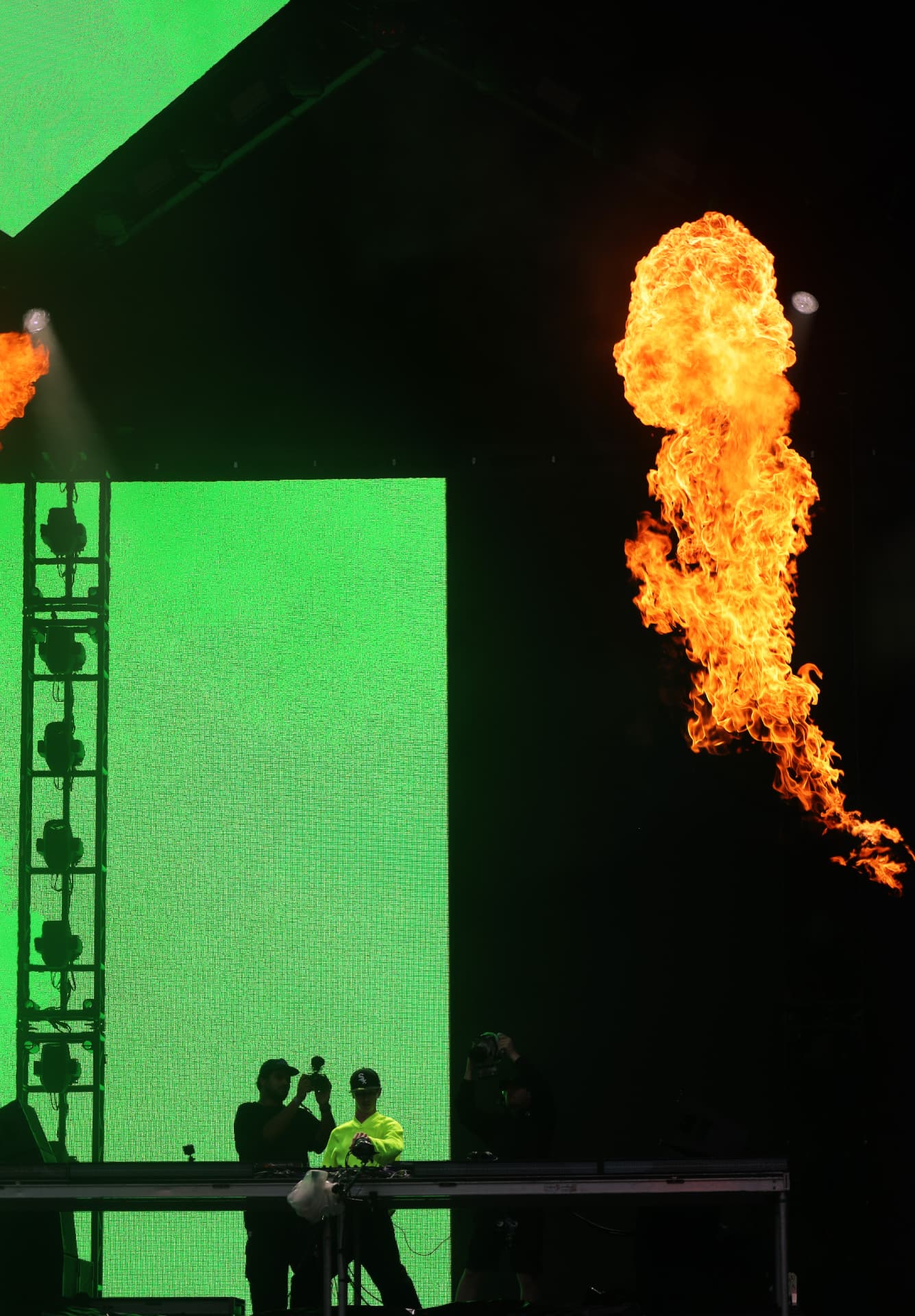 DJ performing on stage with green screen and twin flame jets