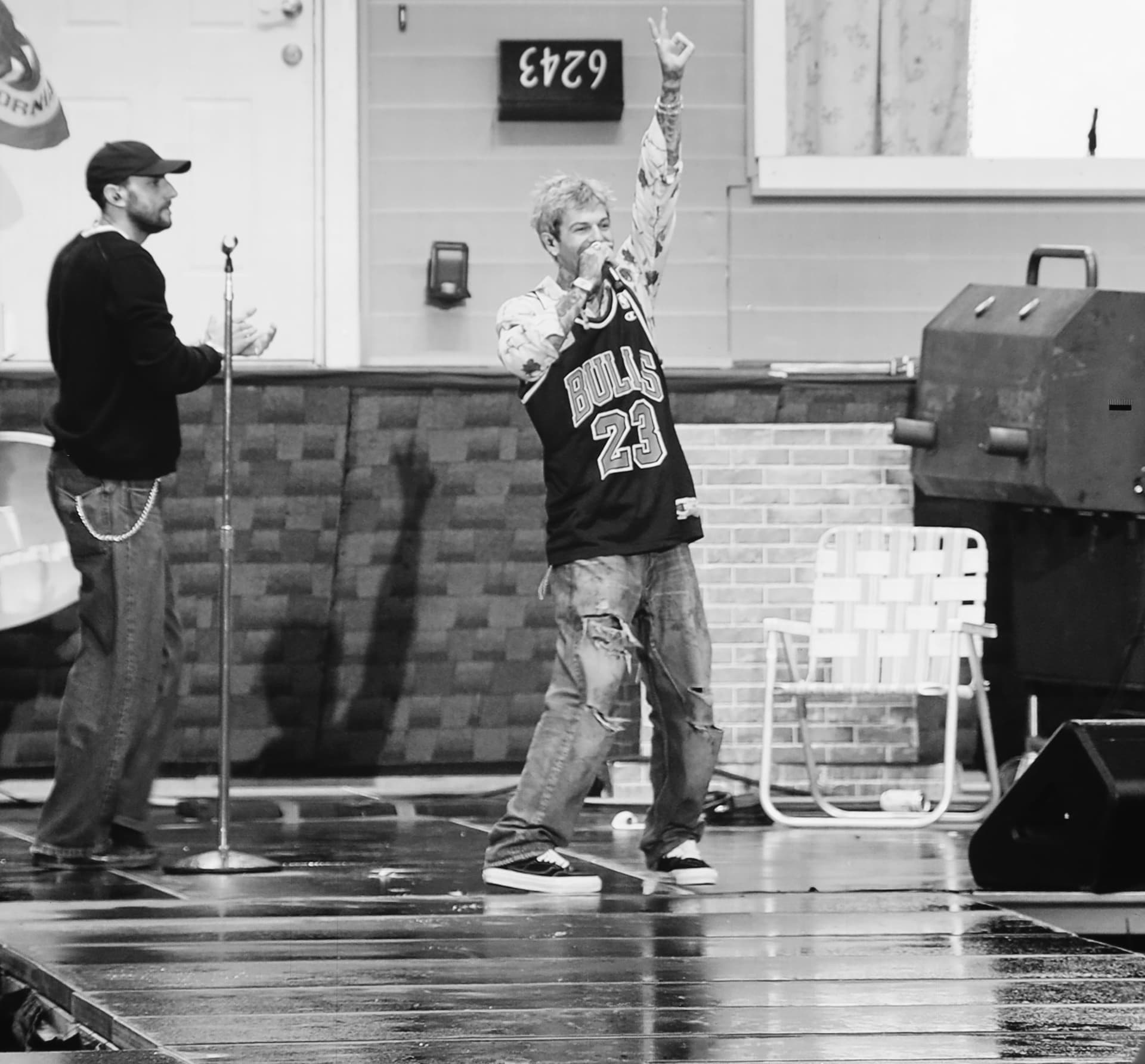 Black and white performer in a Bulls jersey pointing skyward on a rain slick stage