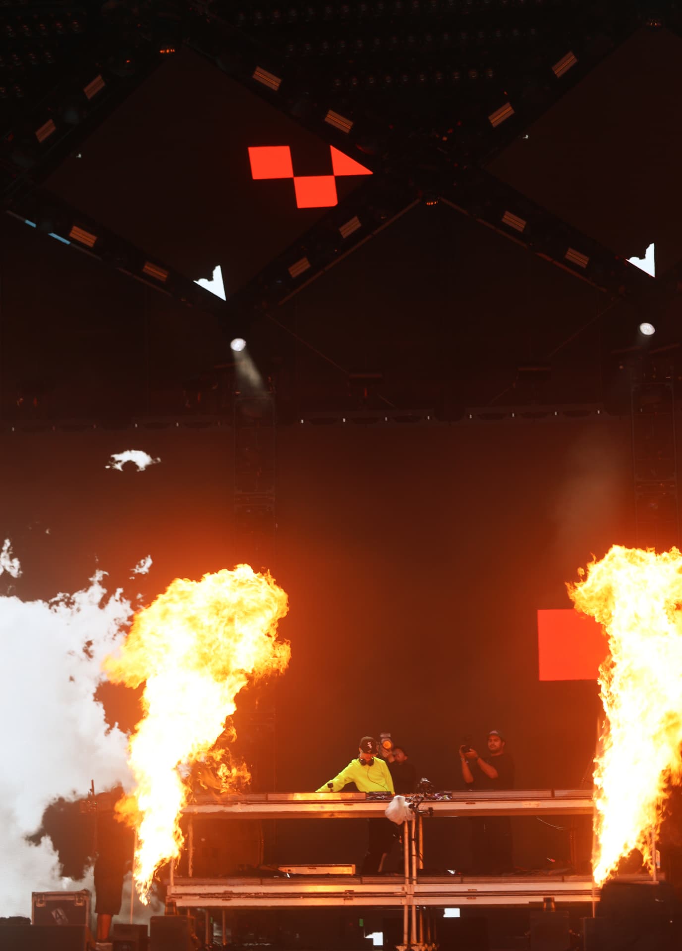 DJ in neon yellow performing between twin flame jets on stage