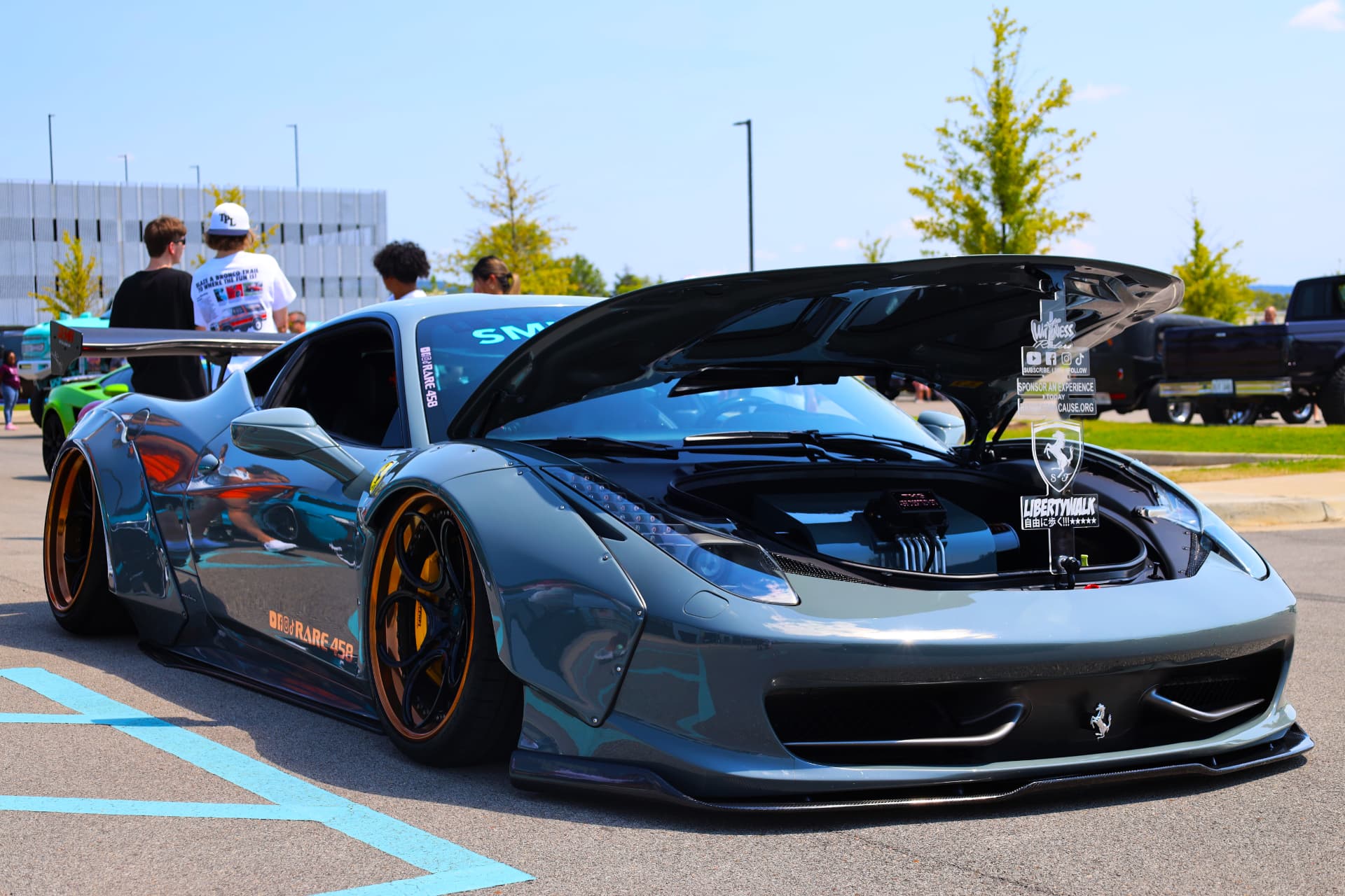 Modified Ferrari 458 with gold wheels and exposed engine at an outdoor car show