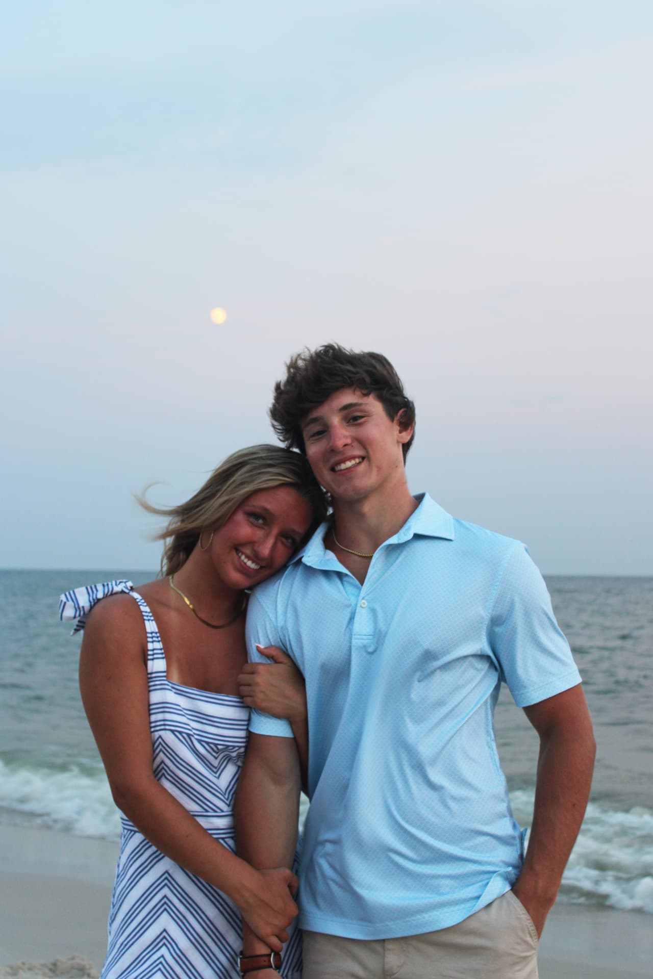 Couple leaning together on the beach beneath a rising moon