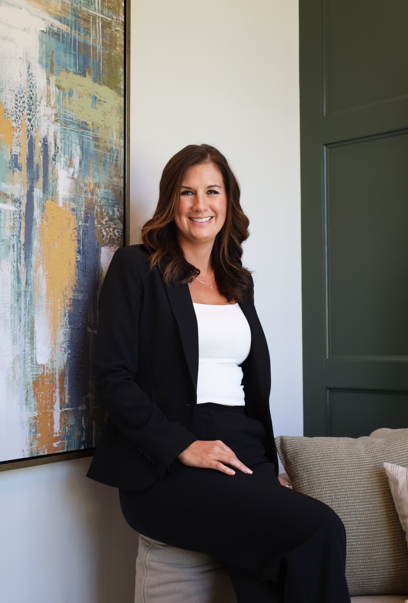 Professional headshot of a woman in a black blazer seated beside abstract art