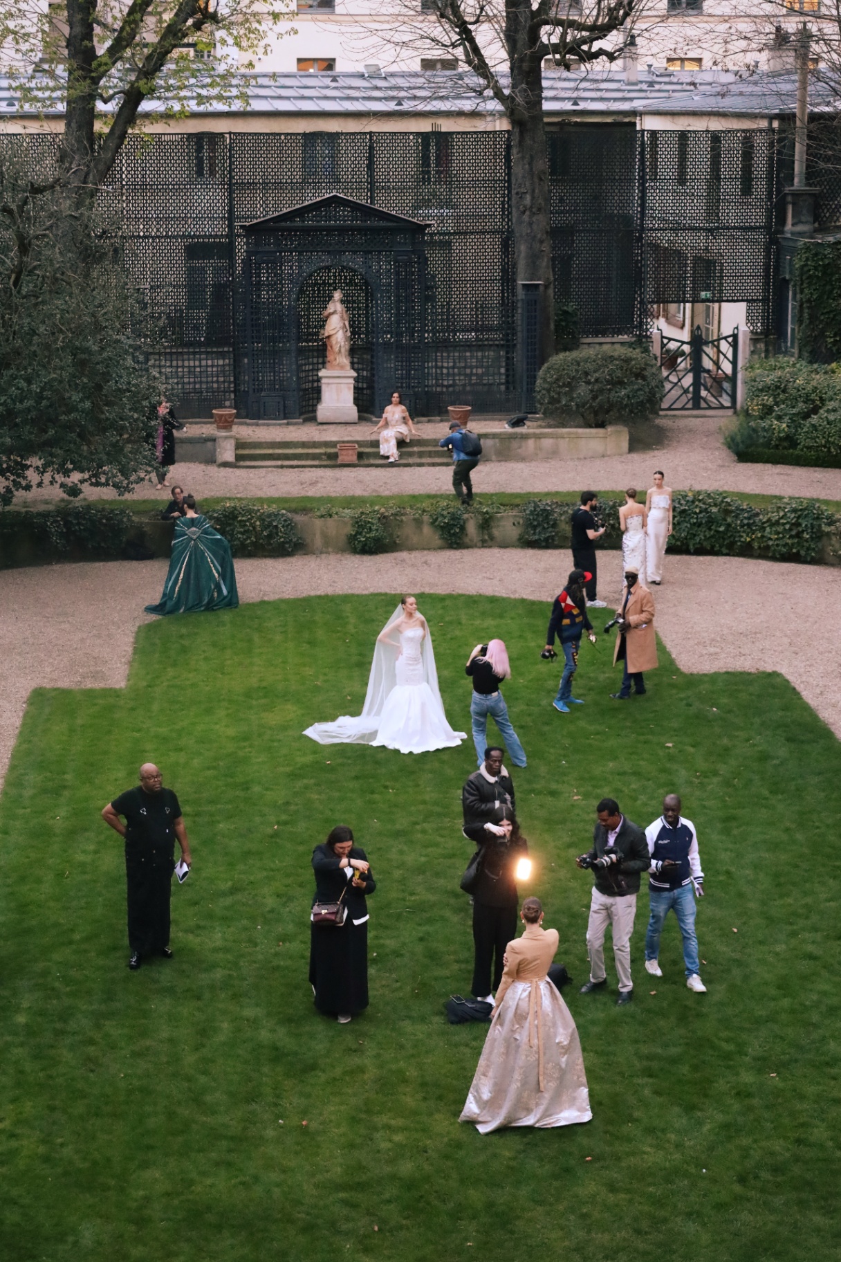 Couture models and photographers gathered in a manicured garden