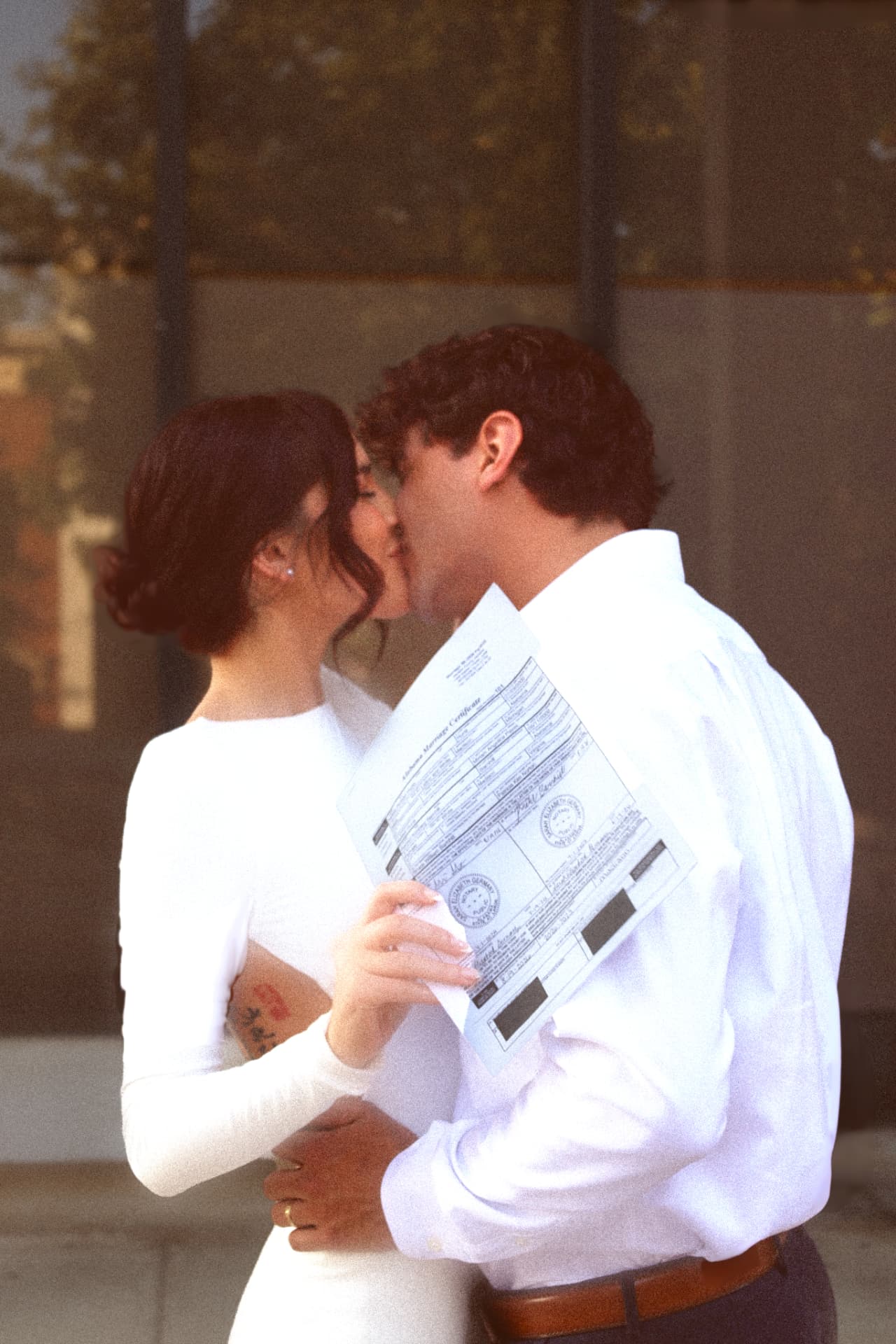 Newlyweds kissing with a marriage certificate reflected in the glass