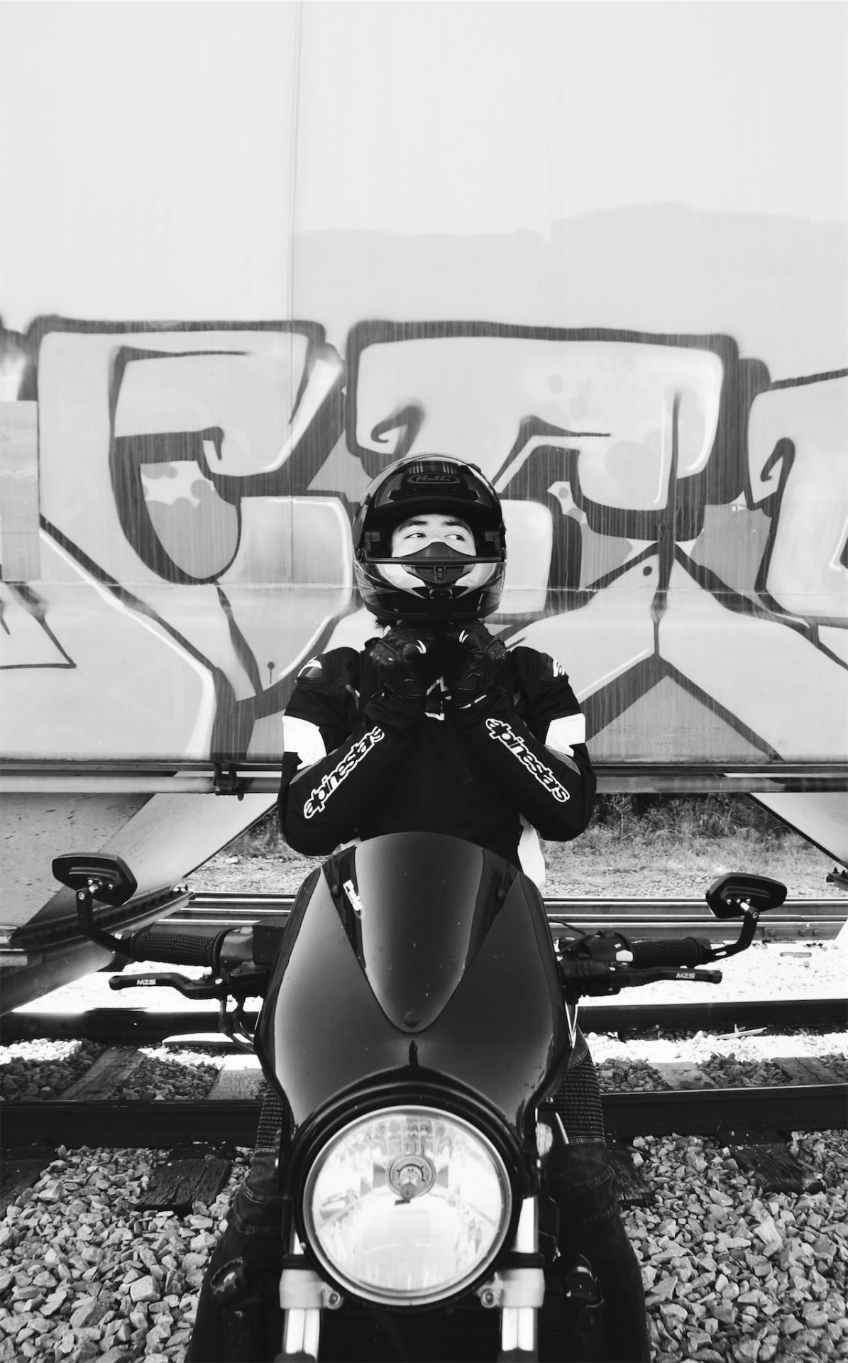 Black and white frame of a rider fastening a helmet in front of a graffiti train car