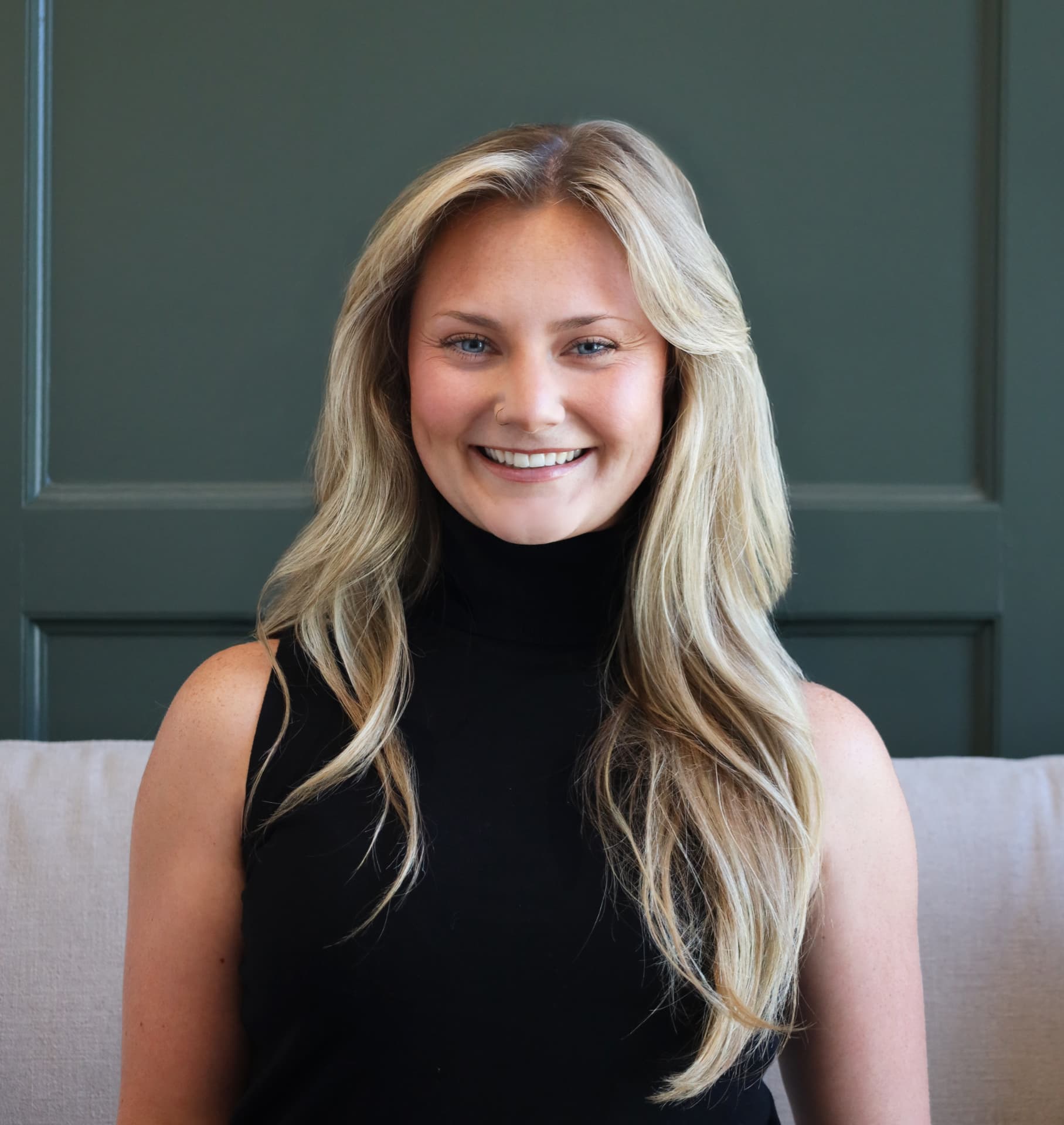 Professional headshot of a woman in a black turtleneck against a deep green backdrop