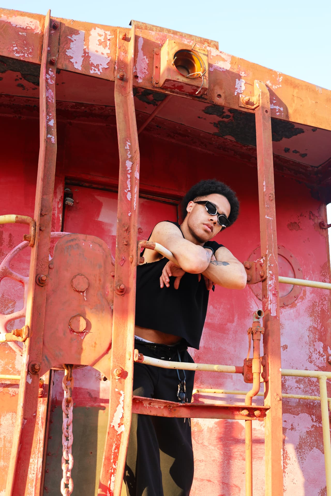 Model in black leaning on the railing of a weathered red caboose