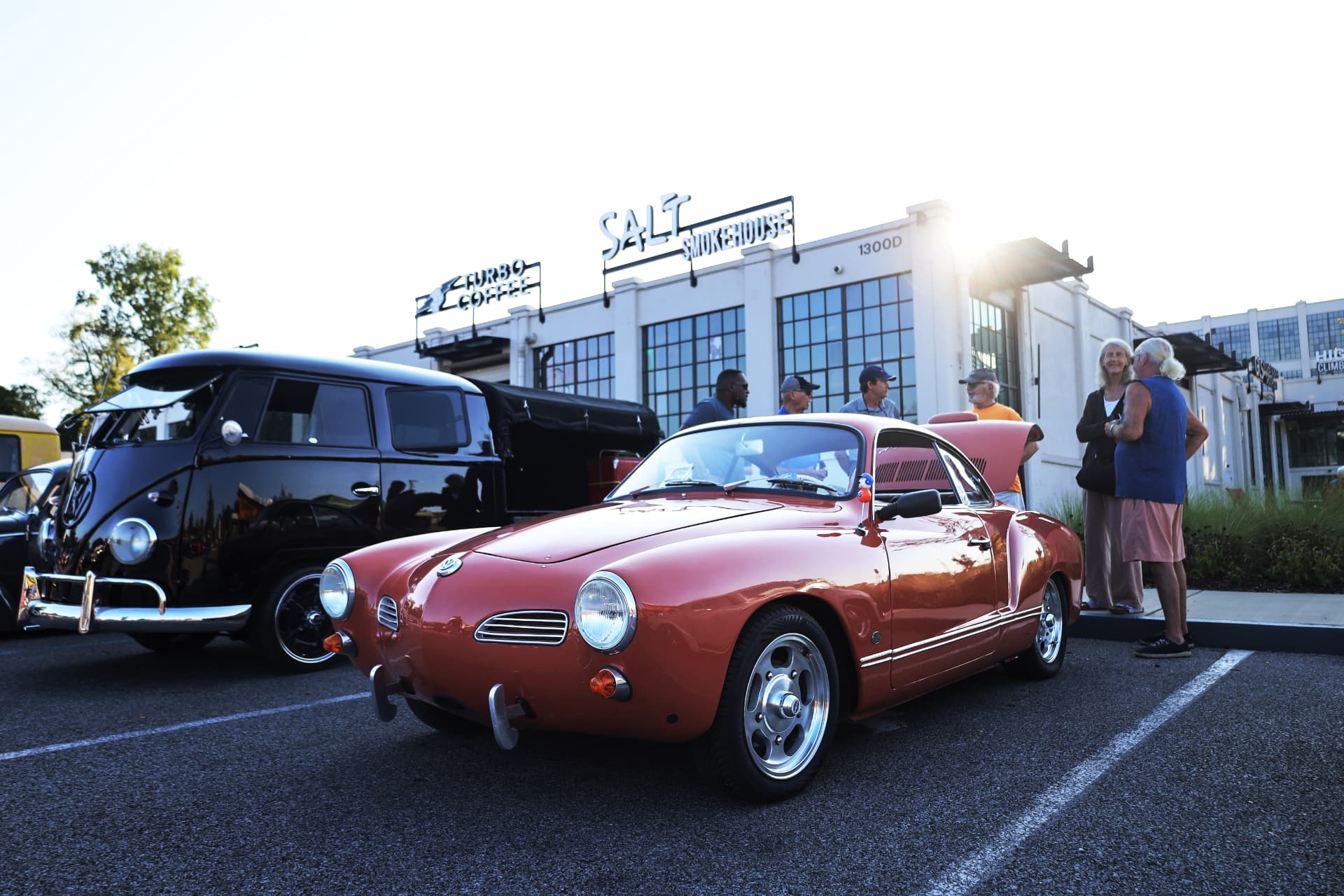 Red Volkswagen Karmann Ghia beside a black VW bus at a cars and coffee
