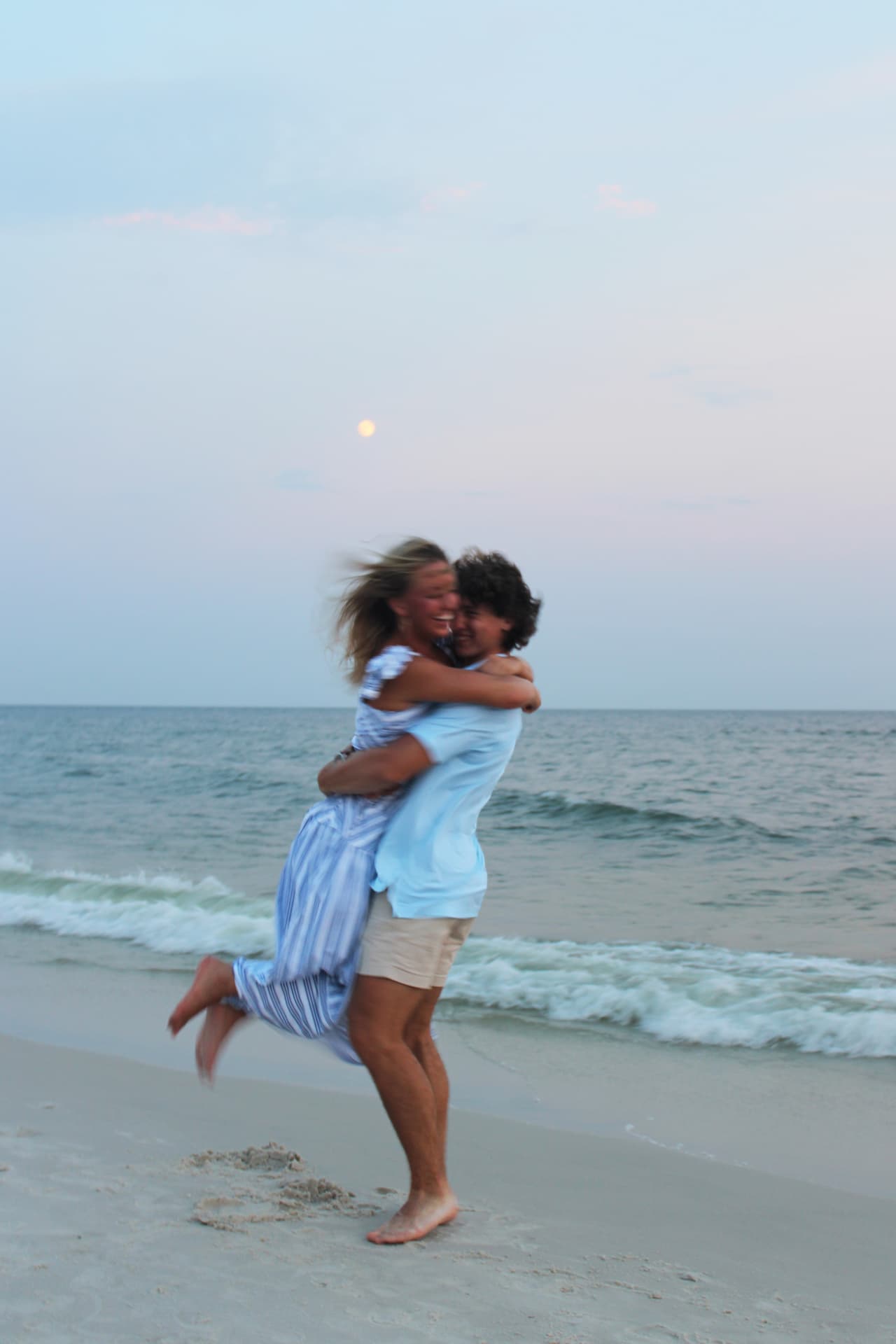 Couple laughing mid-lift on the beach at dusk
