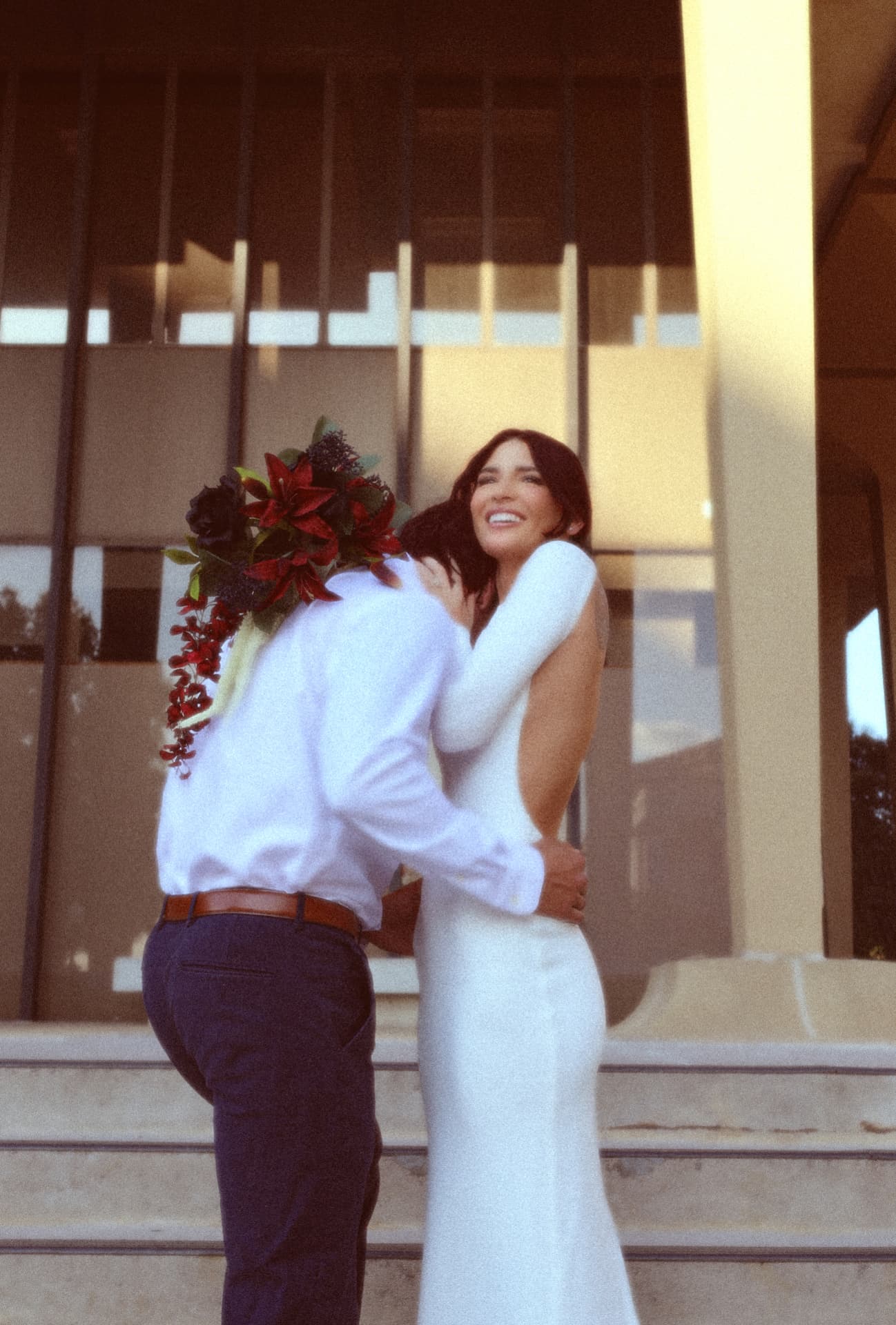 Bride laughing in her groom's arms on sunlit front steps