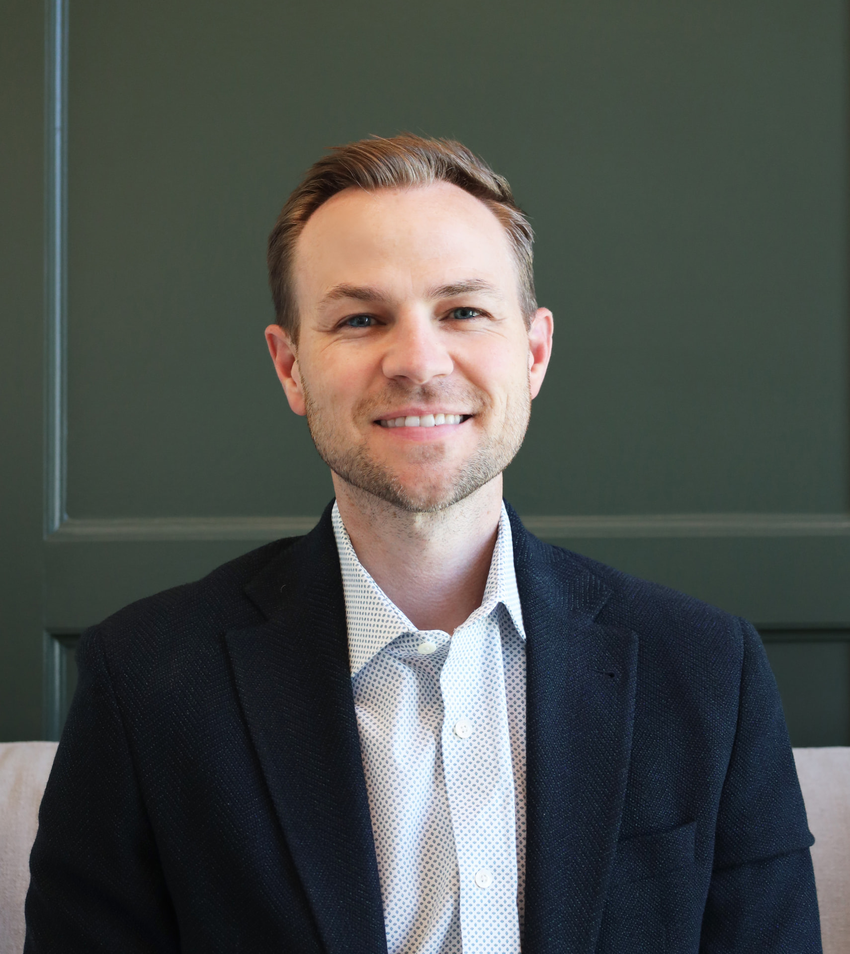 Professional headshot of a man in a dark suit against a deep green backdrop