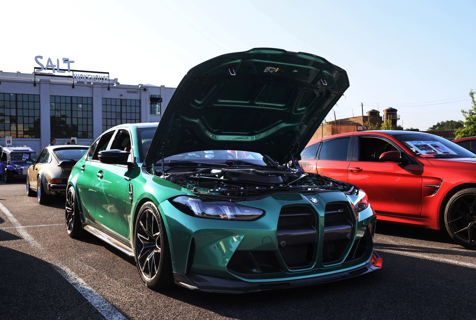 Green BMW M3 with hood open beside a red BMW at Salt Smokehouse cars and coffee