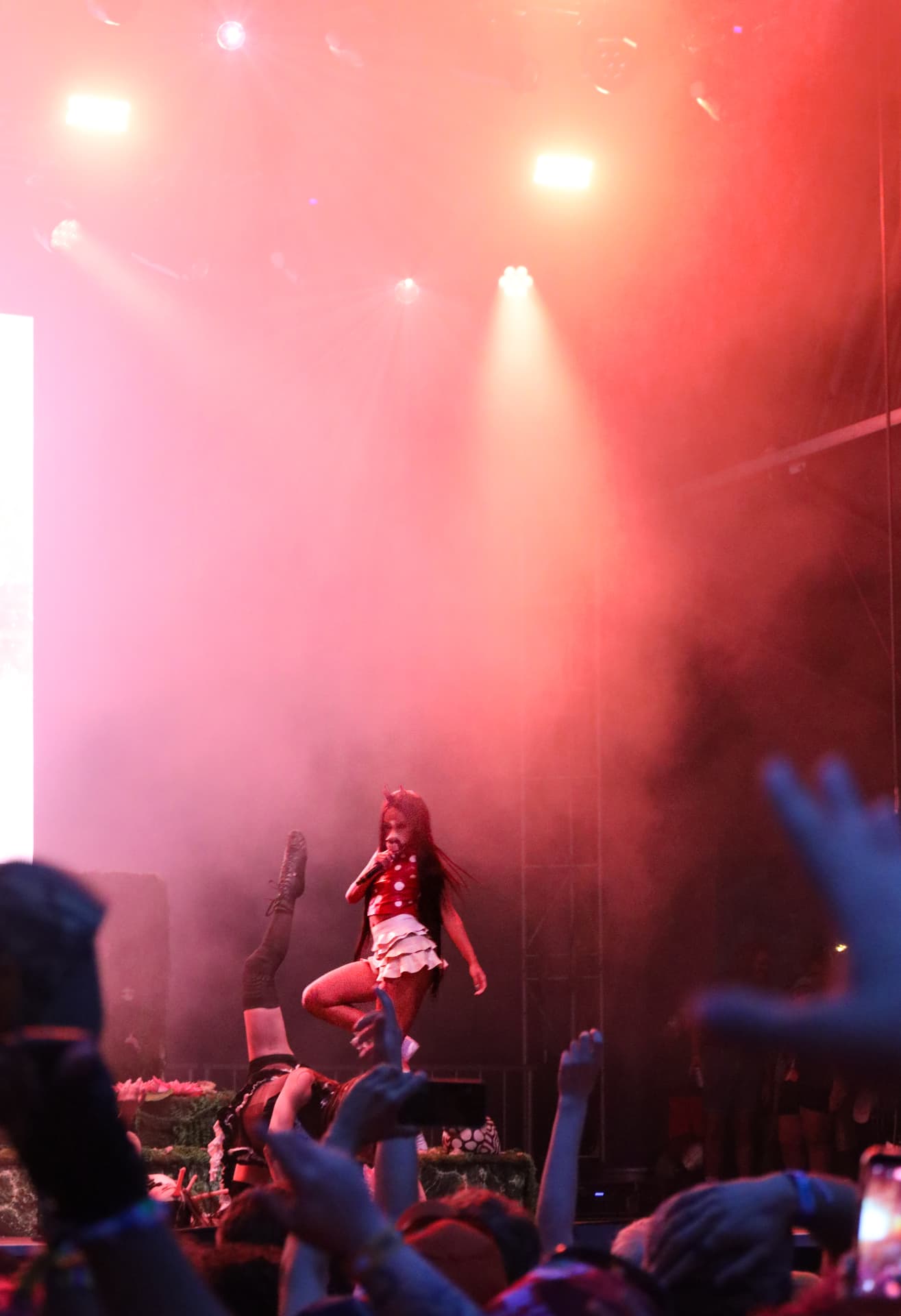 Performer mid movement in red smoke with the crowd's hands raised