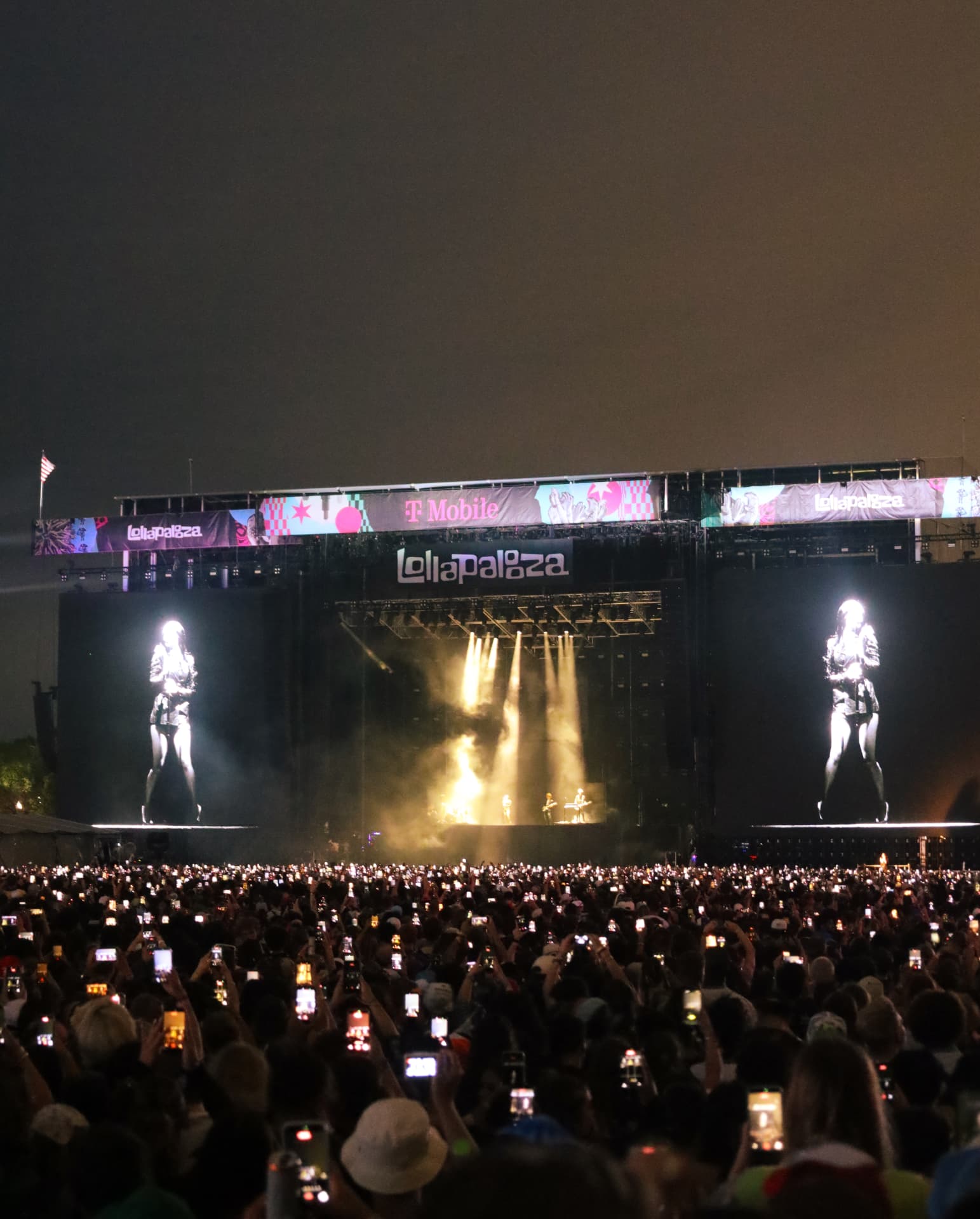 Festival main stage at night with a sea of phone lights in the crowd