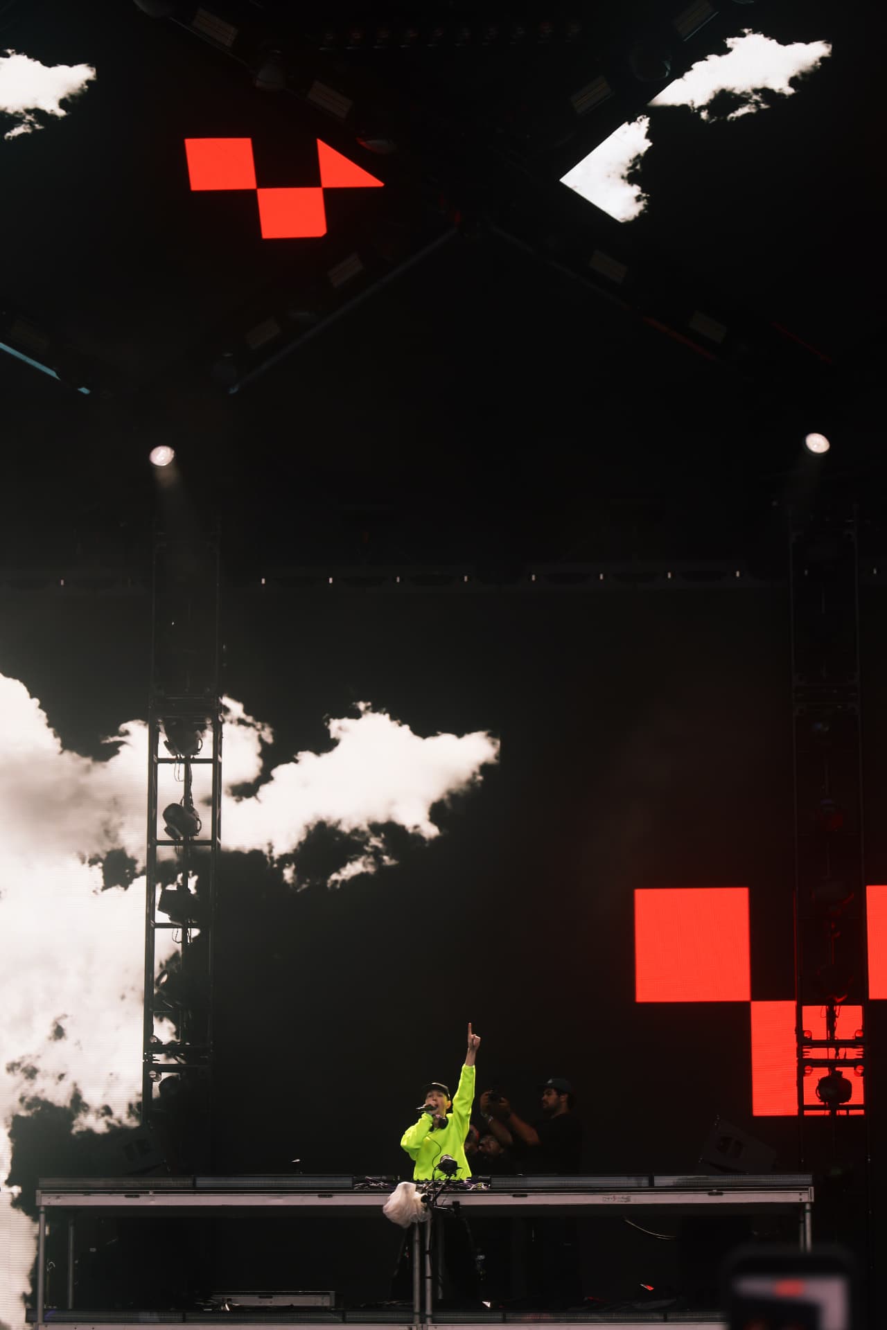 DJ in neon green performing under red geometric screens and stage smoke