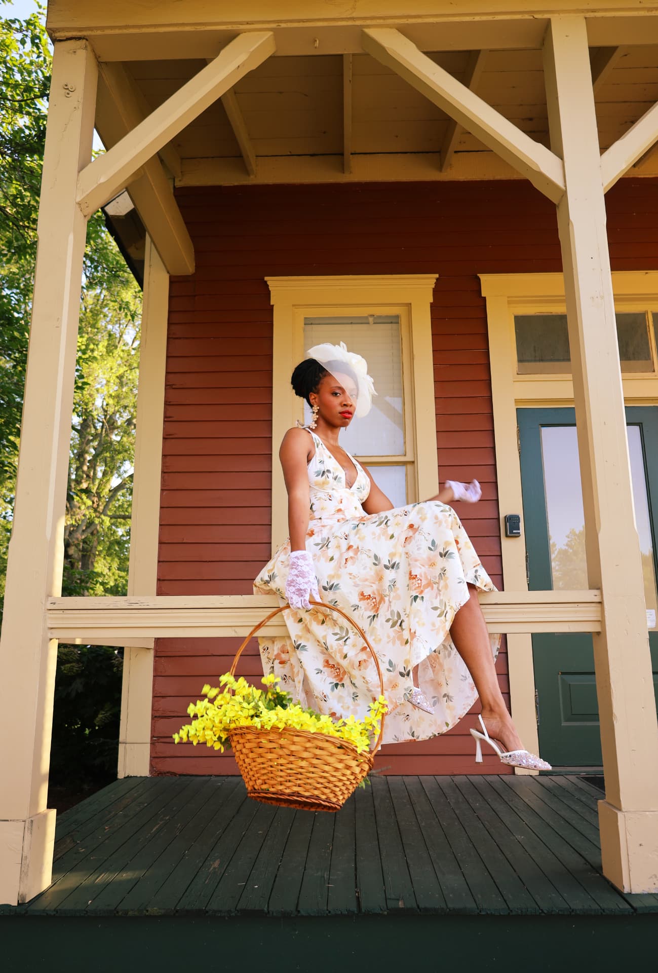 Vintage floral dress portrait on a red porch holding a basket of yellow blooms