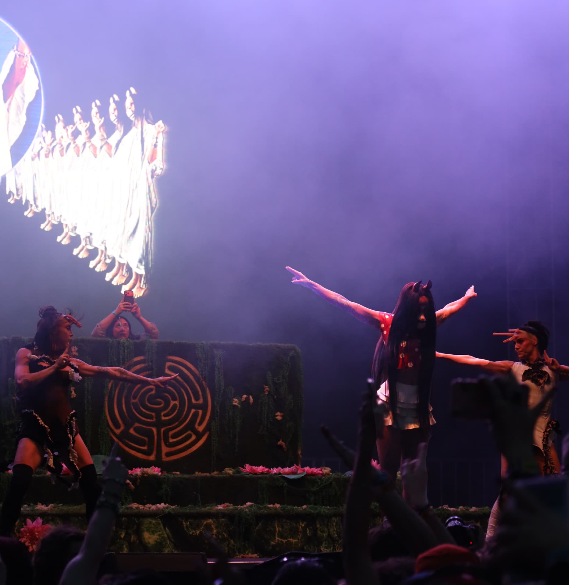 Dancers posed under purple haze before a labyrinth stage set