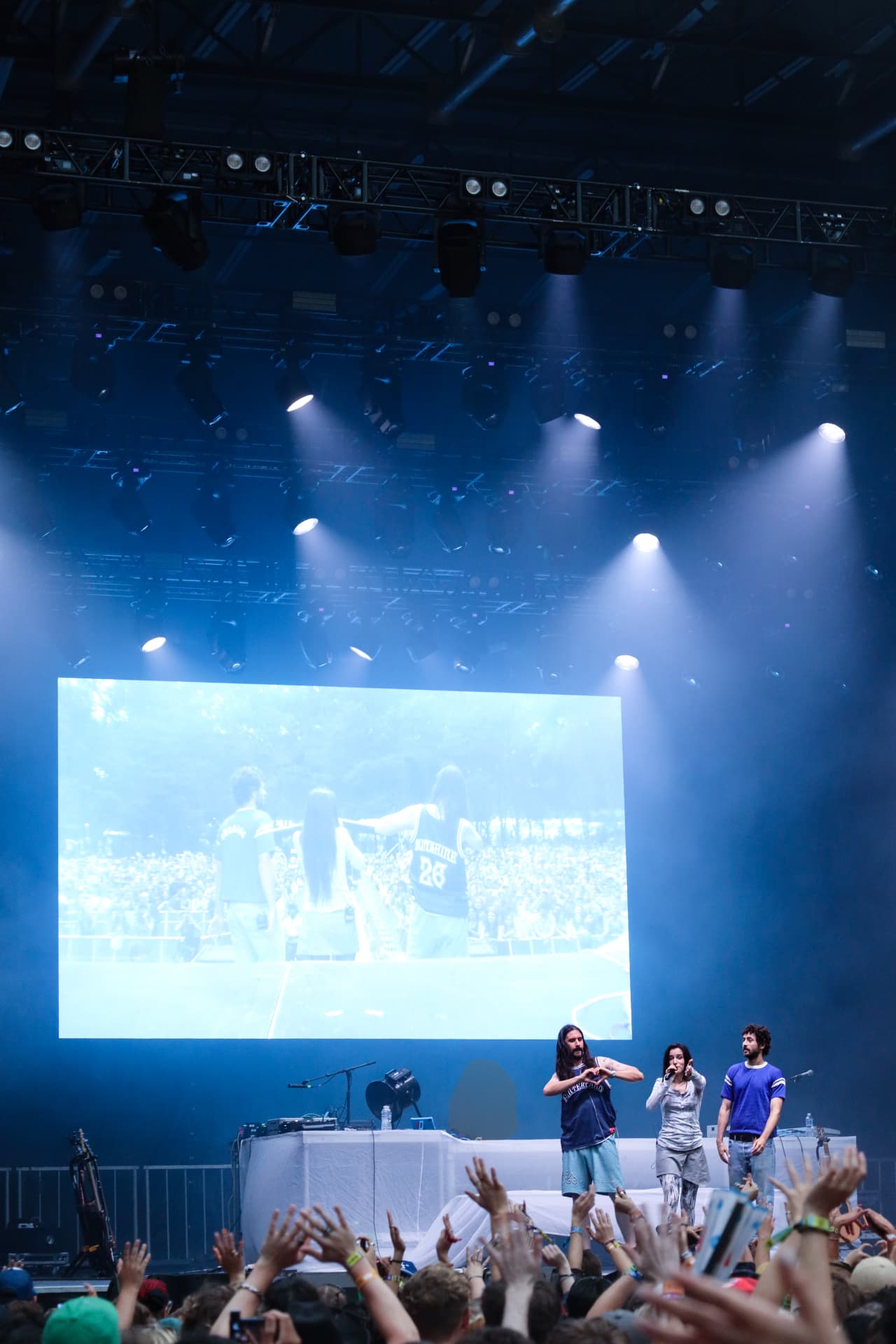 Artists on stage under blue haze with the crowd's hands raised