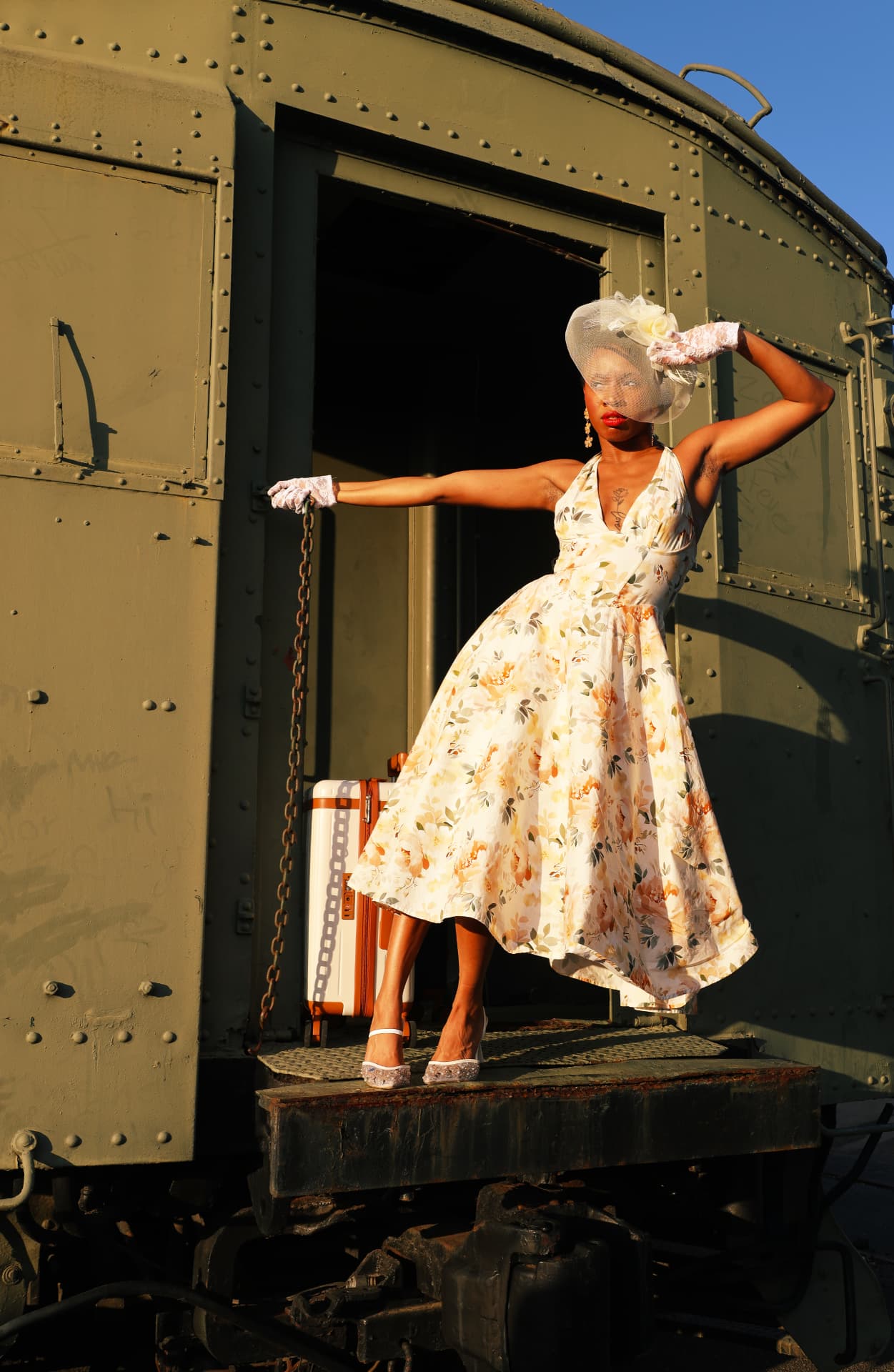 Model in a floral dress and birdcage veil posed on a vintage rail car platform