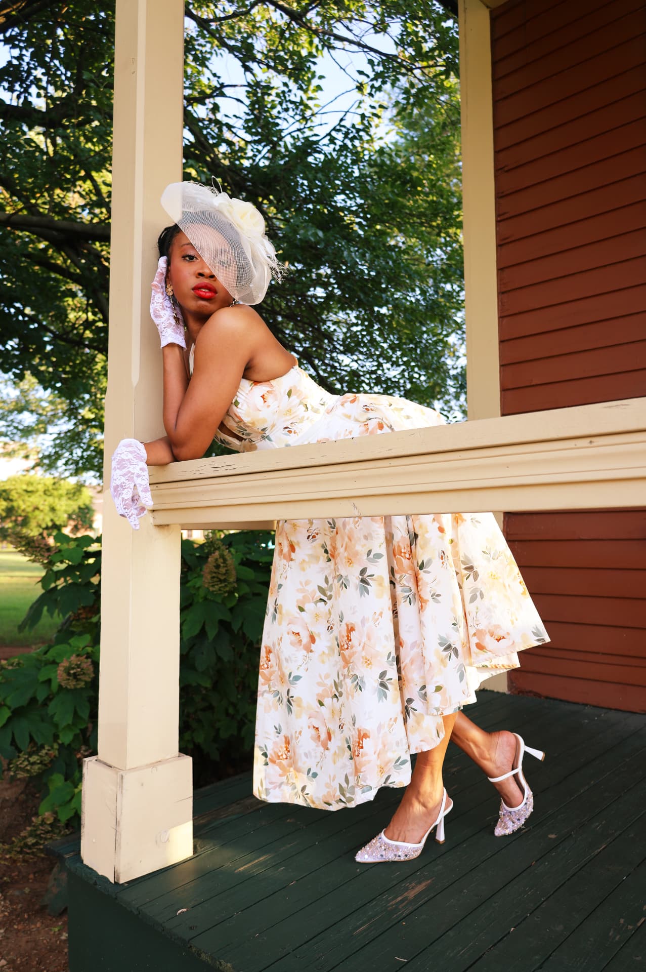 Floral dress and veiled hat portrait leaning along a sunlit porch railing