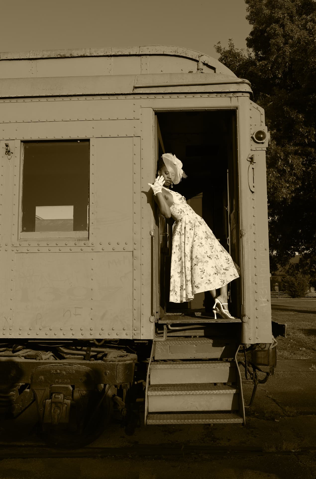Sepia frame of a model in a floral dress leaning in a vintage rail car doorway