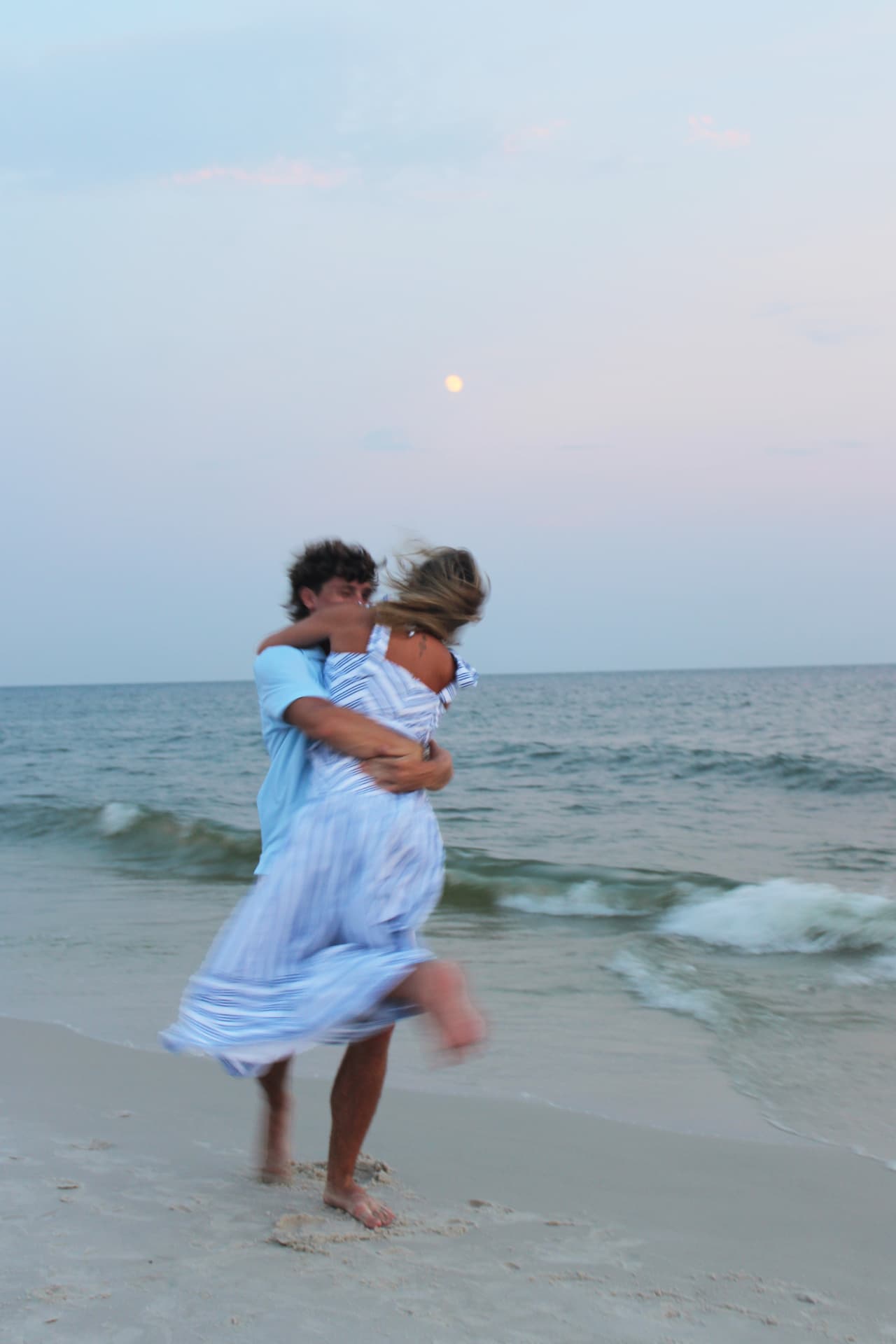 Couple spinning in an embrace on the shoreline under a rising moon