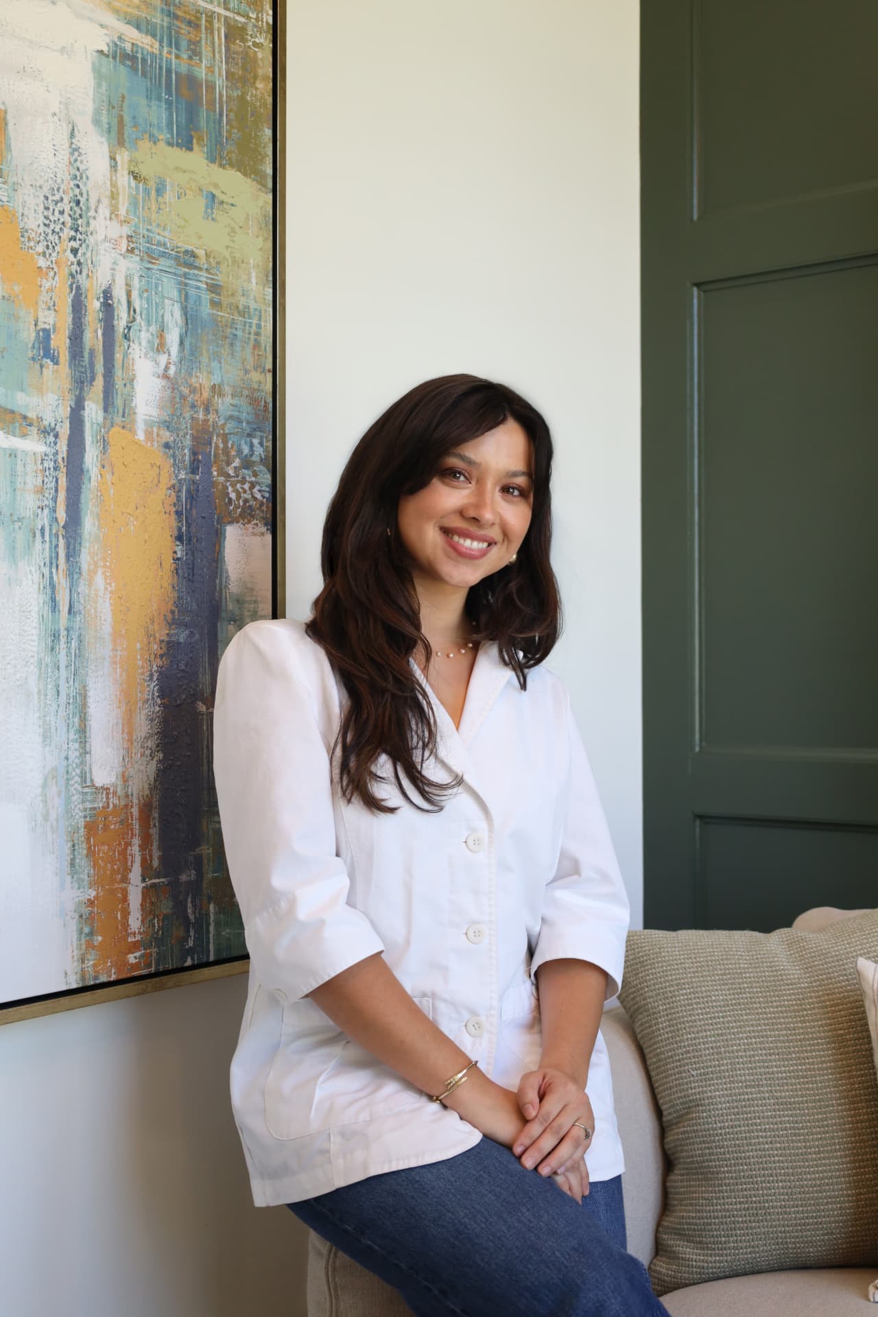 Professional headshot of a woman in a white blouse against a deep green backdrop